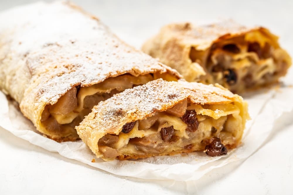 Apfelstrudel aux pommes fondantes et délicatement épicées, enveloppées dans une pâte fine et croustillante.