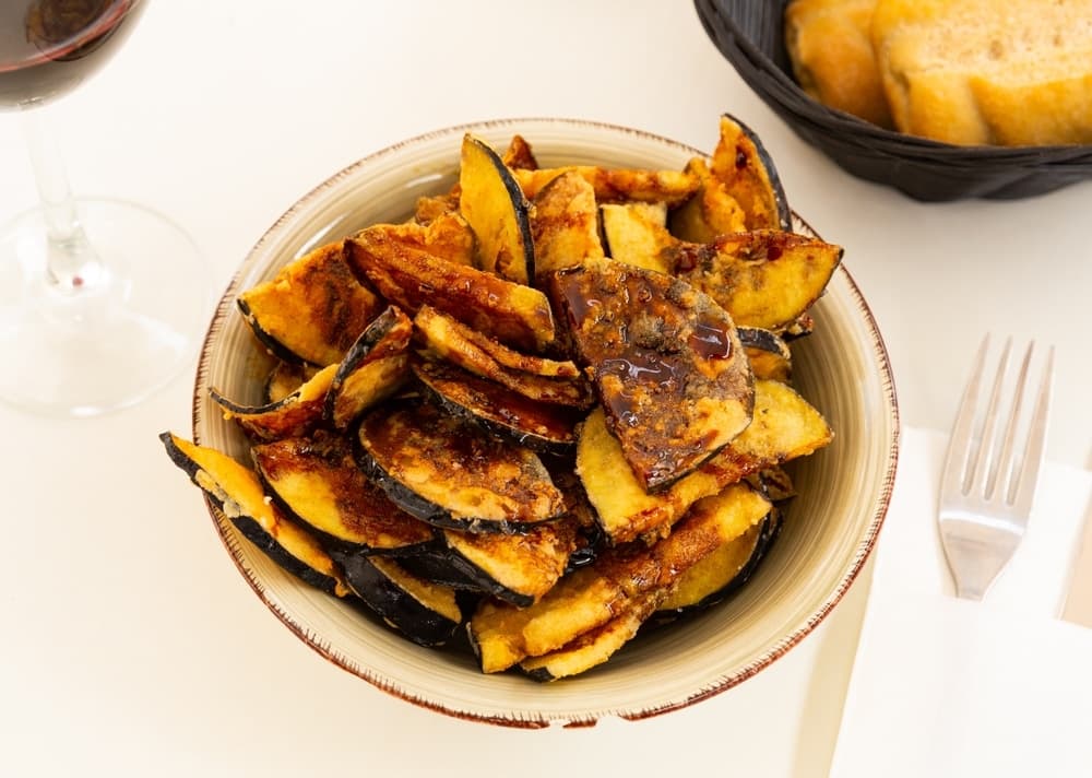 Tapas de berenjenas con miel servies dans un bol, composées d'aubergines frites nappées de miel de canne, une spécialité emblématique de la cuisine andalouse.