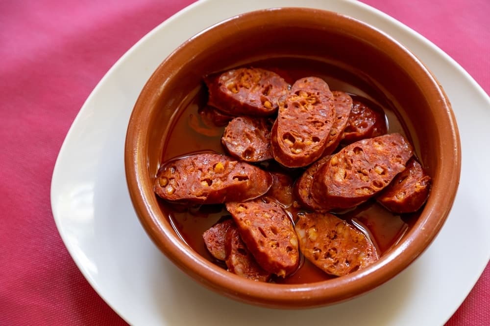 Chorizo a la sidra servi en tapas, préparé avec un chorizo mijoté lentement dans du cidre et accompagné de pain, une spécialité traditionnelle des Asturies en Espagne.