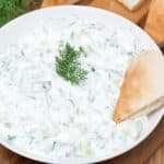 Tzatziki servi dans un bol accompagné de tranches de pain pita.