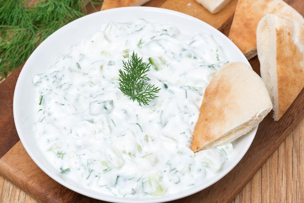 Tzatziki servi dans un bol accompagné de tranches de pain pita.