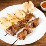 Brochettes d'anticuchos accompagnés de pommes de terre et du maïs.