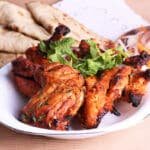 Poulet tandoori servi dans une assiette accompagné de naan et de crudité