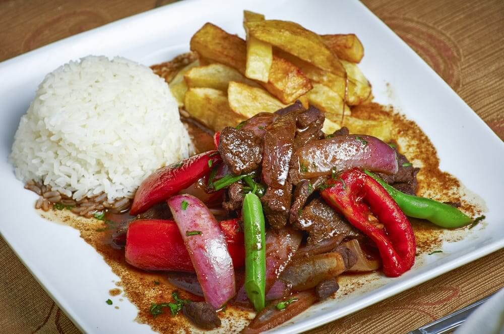 Assiette de lomo saltado péruvien accompagné de frites et de riz blanc