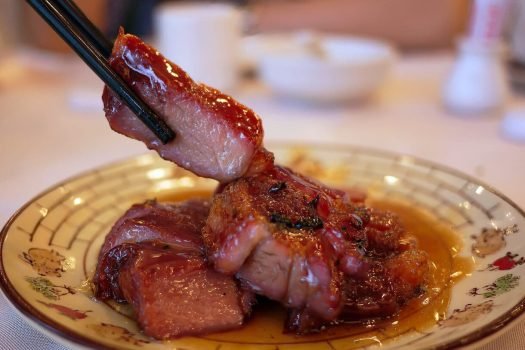 close-up side view chopsticks holding piece of juicy delicious barbecue roasted pork cantonese style